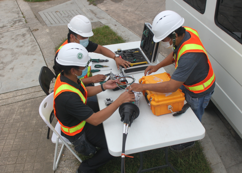 Technicians connecting fiber cables at an outdoor workstation.